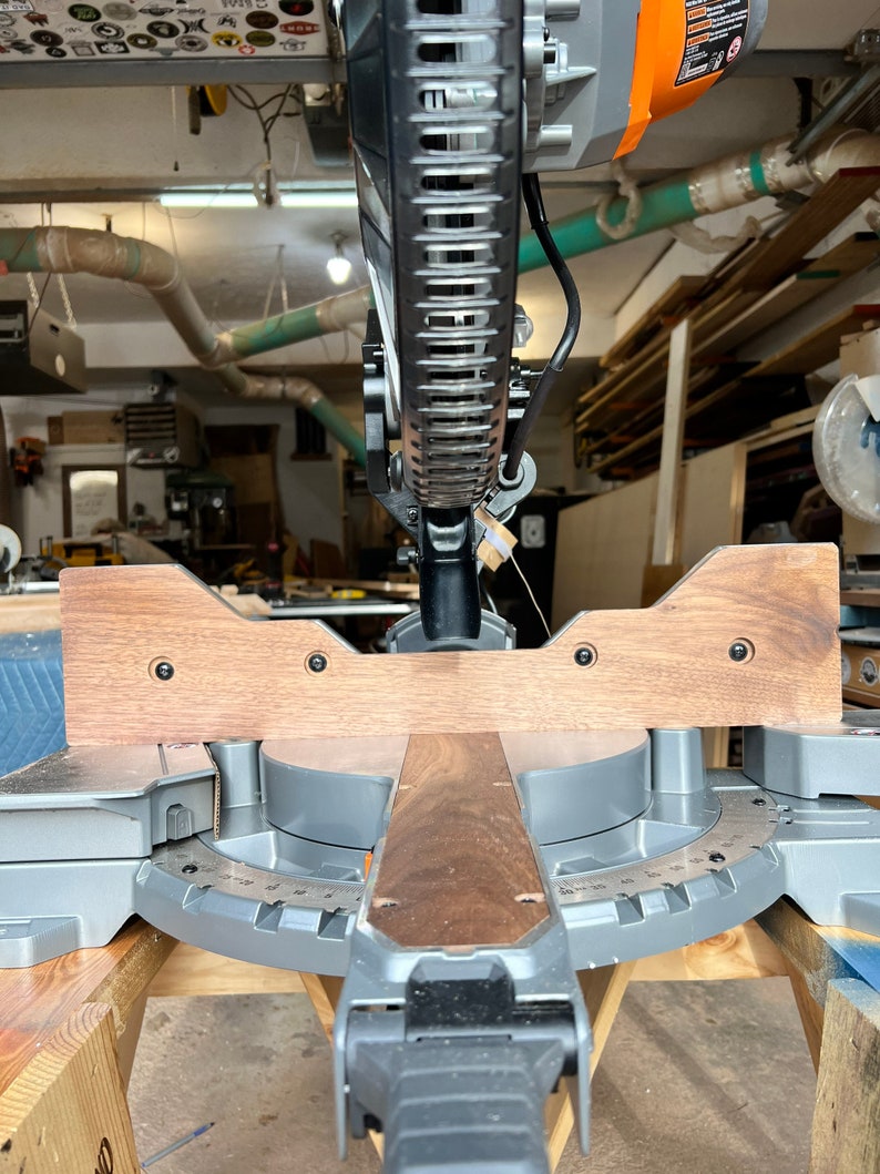 Peut inclure: Vue rapproch&eacute;e d'une scie &agrave; onglets avec une extension en bois fix&eacute;e &agrave; la base. La scie est install&eacute;e sur une table en bois et est pr&ecirc;te &agrave; couper.