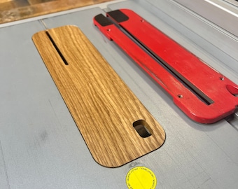 May include: A close-up of a wooden table saw fence with a red and black adjustment lever. The fence is labelled "Precision Cut - Use Soft Pencil -  T-Track Lock - Adjust to Cut Length".