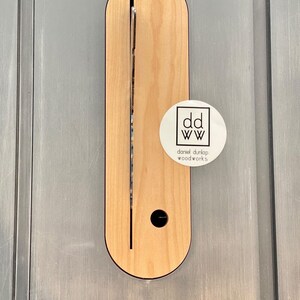 May include: A close-up of a wooden table saw insert with a slot cut into it. The insert is made of light wood and has a dark brown border. A white sticker with the text "dd ww daniel dunlap woodworks" is attached to the insert.