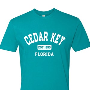 May include: A turquoise blue t-shirt with white text that reads "CEDAR KEY EST 1895 FLORIDA".