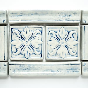 May include: A set of blue and white ceramic tiles with a floral design. The tiles are arranged in a frame shape with two larger tiles in the center.