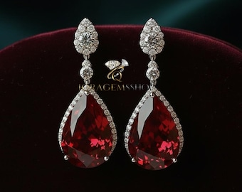 May include: A pair of drop earrings with large, faceted, teardrop-shaped red gemstones. The earrings are adorned with small, sparkling white stones around the red gems and at the top, creating a luxurious design. The earrings are set against a dark background.