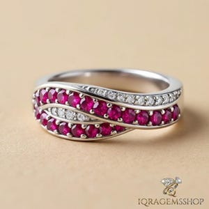 以下が含まれることがあります： 鮮やかな赤い宝石と小さな白い石が並んだ、ダブルバンドデザインのシルバーリング。 リングは光沢のある仕上げで、ニュートラルな背景に配置されています。 リングはジュエリーです。