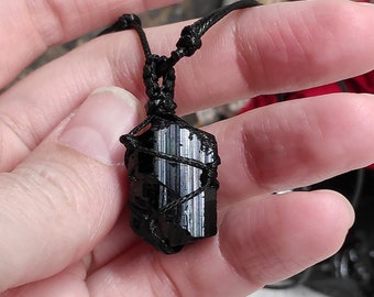 May include: Black tourmaline crystal pendant on a black cord necklace. The crystal is wrapped in black cord and has a natural, raw look.
