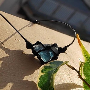 Peut inclure: Un pendentif en cristal bleu enveloppé d'un cordon noir, suspendu à un collier en cordon noir. Le pendentif est noué avec un nœud macramé.