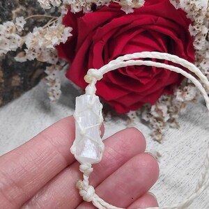 K&ouml;nnte beinhalten: Ein wei&szlig;es Selenit-Kristall, das in wei&szlig;es Makramee-Schnur gewickelt ist, bildet ein Armband. Das Armband ist mit einem Knoten gebunden und wird auf einer Hand gezeigt.