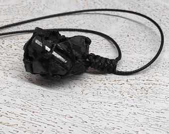 May include: A black obsidian crystal wrapped in black cord, forming a pendant. The crystal has a rough, natural texture and is tied with a simple knot.