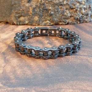 Könnte beinhalten: Ein silberfarbenes Armband im Motorradketten-Design. Das Metallarmband hat einen Verschluss. Die detaillierten Glieder verleihen dem Armband ein robustes, industrielles Aussehen. Das Armband ist ein einzigartiges Accessoire.