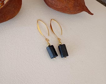 May include: A pair of gold earrings with black rectangular stones hanging from the bottom. The earrings are on a white surface.