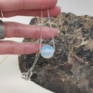 May include: A silver chain necklace with a single, round, iridescent opal pendant.