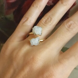 Puede incluir: Un anillo de oro con dos piedras de cristal blancas. El anillo está diseñado para envolverse alrededor del dedo.