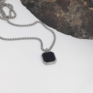 Può includere: Una collana a catena d'argento con un ciondolo ottagonale nero.