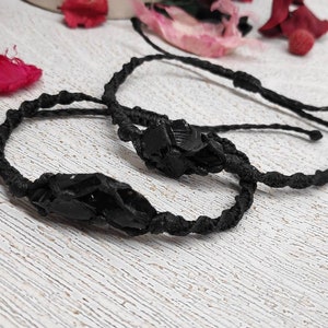 Op de afbeelding: Twee zwarte armbanden met zwarte edelsteenbedels. De armbanden zijn gemaakt van dun zwart koord en zijn aan elkaar gebonden.