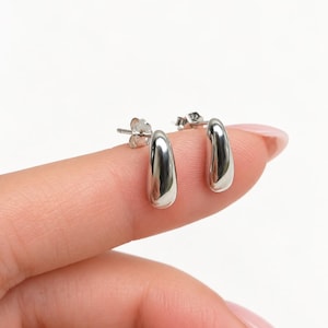 May include: A pair of silver-toned stud earrings featuring a smooth, polished, teardrop-shaped design. Each earring has a reflective metallic surface and includes a standard post back mechanism for secure attachment to the earlobe.