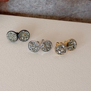 以下が含まれることがあります： キラキラと輝く金属製の仕上げが施された、小さな丸いイヤリングのセットです。イヤリングは、シルバー、ゴールド、ブラックの3色展開です。