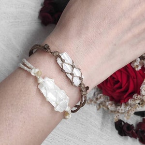K&ouml;nnte beinhalten: Zwei Armb&auml;nder mit wei&szlig;en Selenit-Kristallspitzen, die in braunes Band gewickelt sind. Die Armb&auml;nder werden am Handgelenk einer Person getragen.