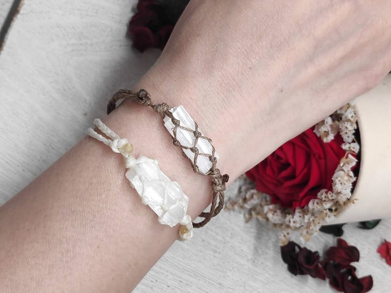 K&ouml;nnte beinhalten: Zwei Armb&auml;nder mit wei&szlig;en Selenit-Kristallspitzen, die in braunes Band gewickelt sind. Die Armb&auml;nder werden am Handgelenk einer Person getragen.