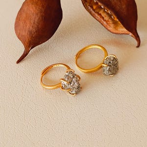 Peut inclure: Deux boucles d'oreilles créoles en or avec une pierre grise scintillante au centre de chaque créole.