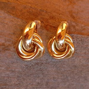 Peut inclure: Une paire de boucles d'oreilles en forme de nœud en or. Les boucles d'oreilles sont en métal épais et brillant et ont un design simple et élégant.
