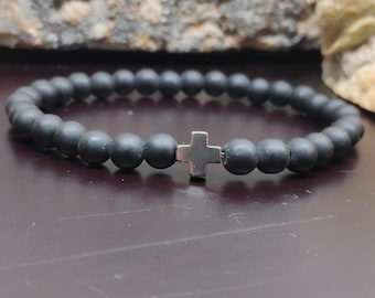 May include: A black beaded bracelet with a silver cross charm. The bracelet is made of matte black beads and has a simple, elegant design.
