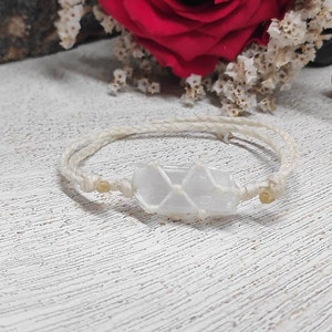 K&ouml;nnte beinhalten: Ein wei&szlig;es Kristall-Armband mit einem wei&szlig;en Band und goldenen Perlen. Der Kristall ist klar, wei&szlig; und durchscheinend.