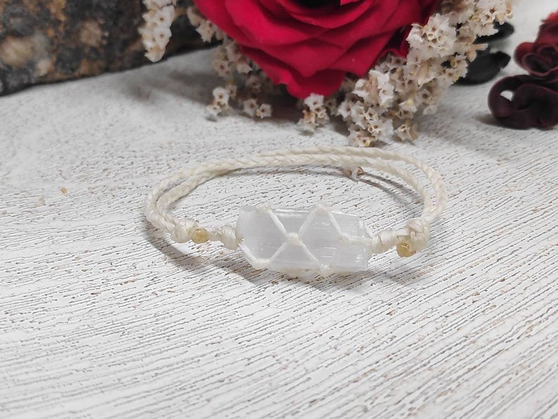 K&ouml;nnte beinhalten: Ein wei&szlig;es Kristall-Armband mit einem wei&szlig;en Band und goldenen Perlen. Der Kristall ist klar, wei&szlig; und durchscheinend.