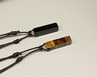 May include: Two necklaces with black cords and rectangular pendants. One pendant is black and the other is brown with gold streaks.
