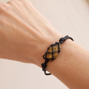 May include: A black cord bracelet with a brown tiger's eye stone wrapped in black cord.