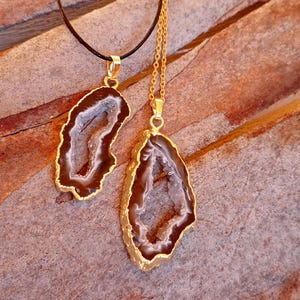 May include: Two agate pendant necklaces with gold-plated settings. The larger pendant is on a black cord, and the smaller pendant is on a gold chain.