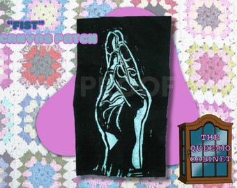 May include: Black canvas patch with a light blue hand illustration. The patch has the text "FIST" and "CANVAS PATCH" in a light purple color. The background includes a pink shape and a colorful patchwork design.