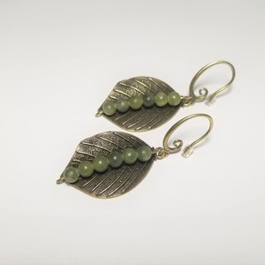 Puede incluir: Un par de pendientes de hoja de latón y piedra verde. Los pendientes presentan un delicado diseño de hoja con una fila de piedras verdes.