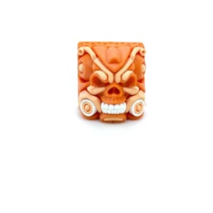 Puede incluir: Un tapón de tecla naranja y blanco con un diseño de calavera. La calavera tiene un diseño detallado con líneas y patrones intrincados.