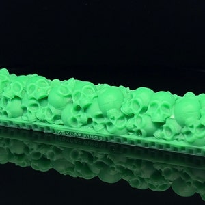 Puede incluir: Un tapón de tecla de plástico verde con un diseño de calavera. El tapón de tecla está hecho por Keycap Kings.
