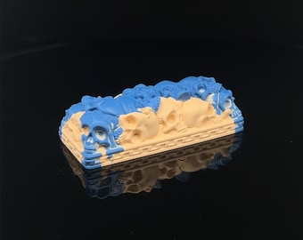 Könnte beinhalten: Ein blauer und beiger 3D-gedruckter Keycap mit einem Totenkopfdesign. Der Keycap ist aus Harz gefertigt und hat eine glatte Oberfläche.
