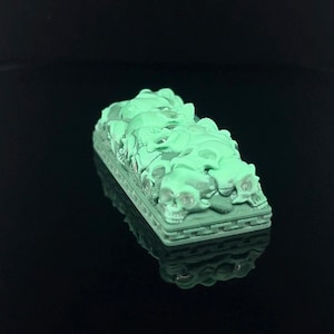 Puede incluir: Un tapón de tecla impreso en 3D de color verde con un diseño de calaveras apiladas.