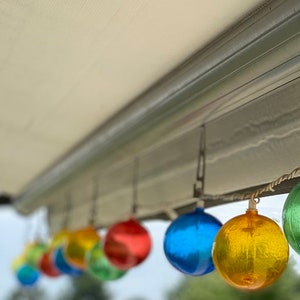 May include: A string of colorful glass globe lights hanging from a white awning. The globes are red, orange, yellow, green, blue, and purple.