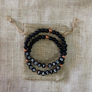 May include: Two black beaded bracelets with copper accents. The beads spell out "Hungry Dogs Run Faster".