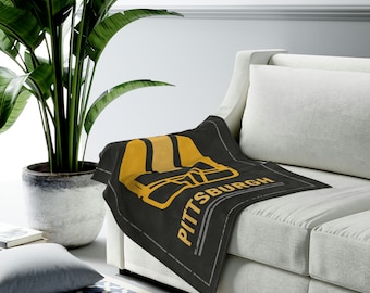 May include: A black and yellow throw blanket with a football helmet graphic and the text "PITTSBURGH" on a white couch.