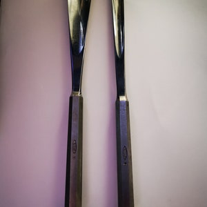 May include: Two silver metal wood carving tools with a rounded tip and a hexagonal handle. The tools have a star and a small oval with text on the handle.