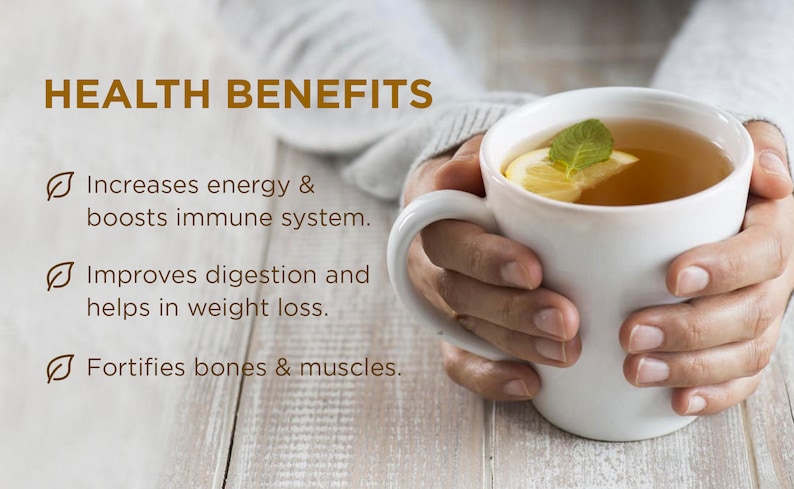 May include: A white mug with a lemon slice and a sprig of mint in it. The mug is filled with a light brown liquid. The text "HEALTH BENEFITS" is at the top of the image. Below the mug, there are three bullet points with check marks. The bullet points list the health benefits of the drink: increases energy and boosts the immune system, improves digestion and helps with weight loss, and fortifies bones and muscles.