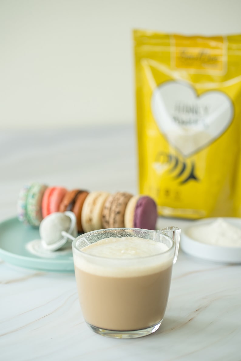 May include: A glass of coffee with a layer of foam on top, next to a plate of colorful macarons and a bag of gluten-free baking mix.