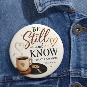 Puede incluir: Un botón redondo con fondo crema y el texto marrón "BE Still and KNOW THAT I AM GOD. PSALM 46:10". El diseño incluye una taza de café color canela con un corazón, vapor formando un corazón, un disco de vinilo negro y corazones pequeños.