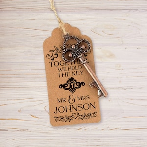 Puede incluir: Una etiqueta de papel marr&oacute;n con un abridor de botellas con forma de llave decorativa. La etiqueta dice "Together we hold the key" y "Mr & Mrs Johnson".