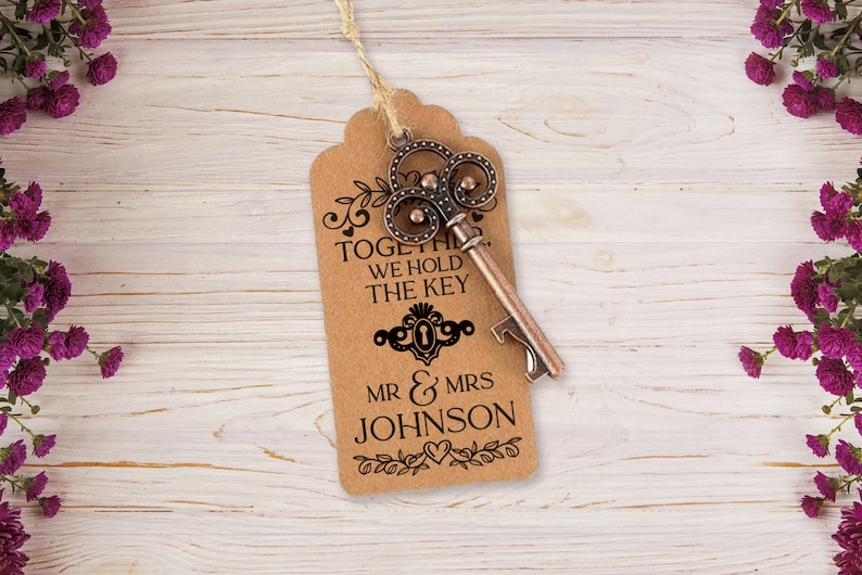 Puede incluir: Una etiqueta de papel marr&oacute;n con un abridor de botellas con forma de llave decorativa. La etiqueta dice "Together we hold the key" y "Mr & Mrs Johnson".
