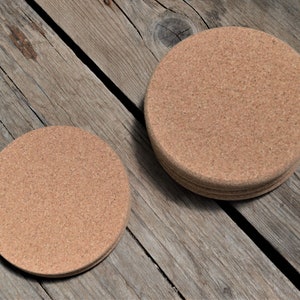 May include: Two round cork coasters, one stacked on top of the other, on a wooden surface. The larger coaster is about 4 inches in diameter.