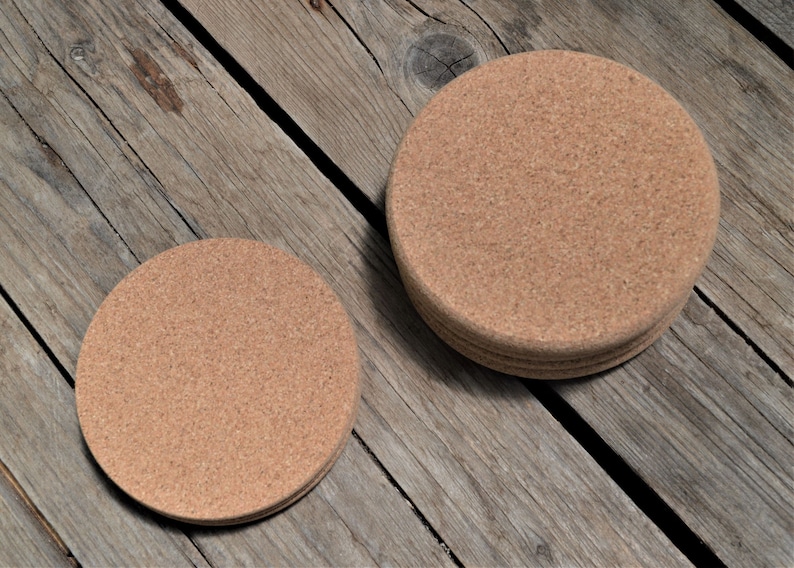 May include: Two round cork coasters, one stacked on top of the other, on a wooden surface. The larger coaster is about 4 inches in diameter.