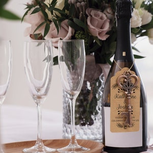 Puede incluir: Una botella de champ&aacute;n con un abridor de botellas de llave dorada adjunto. La etiqueta en el abridor de botellas dice "Katherine & Joshua" y "Gracias por celebrar con nosotros".