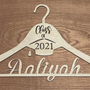 May include: A wooden hanger with the text "Class of 2021" and a graduation cap design. The name "Aaliyah" is written in cursive on the bottom of the hanger.