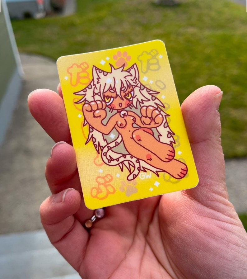 May include: A yellow sticker with a cartoon illustration of a white cat with a pink nose and yellow eyes. The cat is wearing a pink collar with a white gem. The cat is surrounded by yellow stars and paw prints. The sticker has the text "GW" in the bottom right corner.