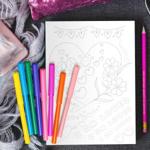 May include: A coloring page with a heart shape and the text "I am loved" repeated three times. The heart is decorated with flowers, birds, and hearts. The page is surrounded by a set of ten colorful markers.